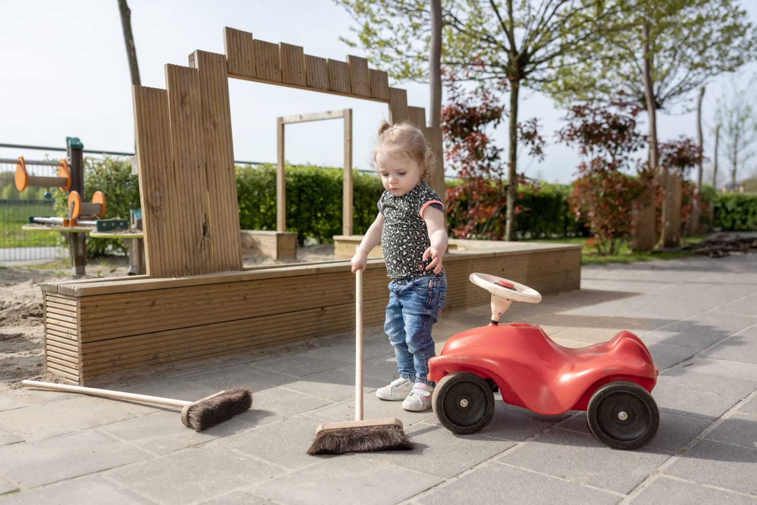 Kind speelt buiten met een bezem bij kinderopvang Kind&co ludens