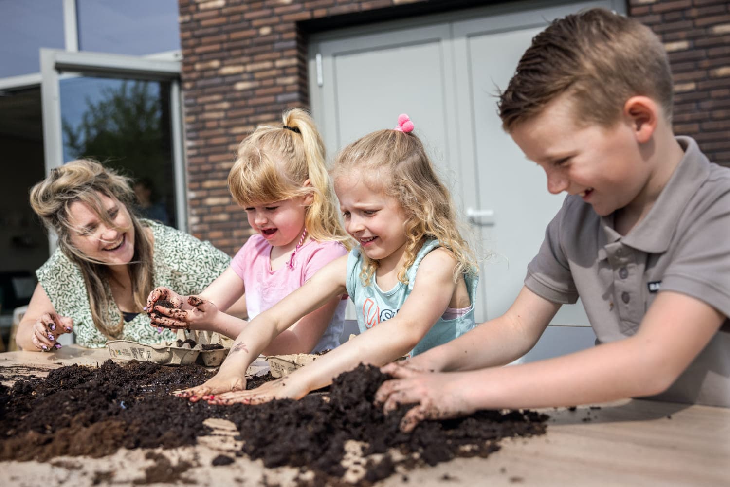 Kinderen tuinieren met pedagogisch medewerker bij kinderopvang Kind&co ludens