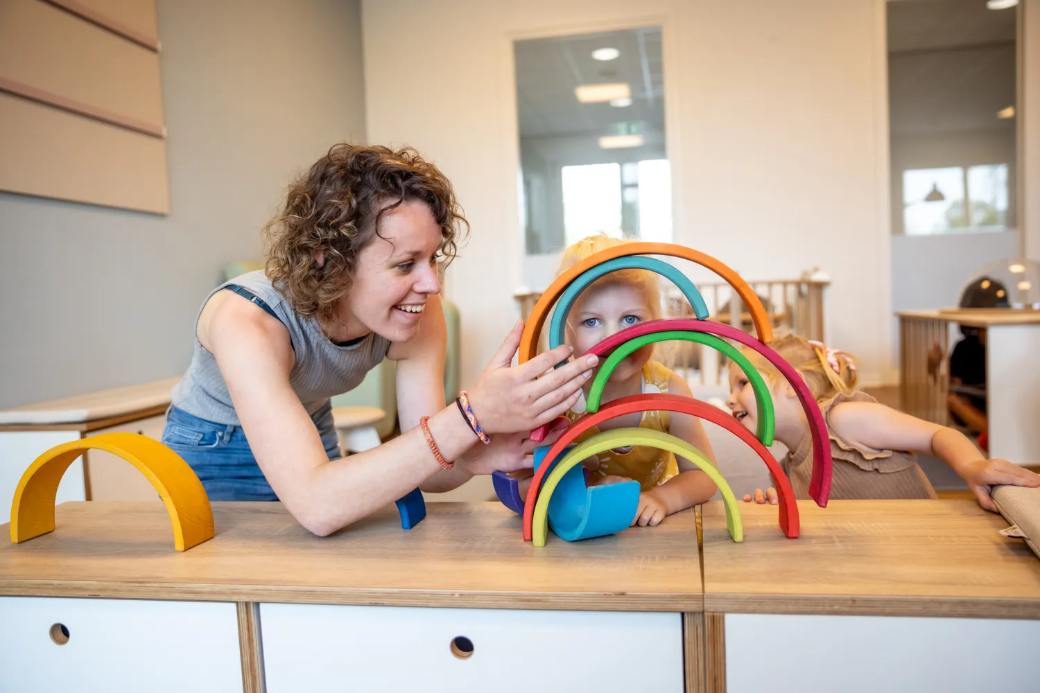 Kind stapelt houten regenboog samen met pedagogisch medewerker bij kinderopvang Kind&co ludens