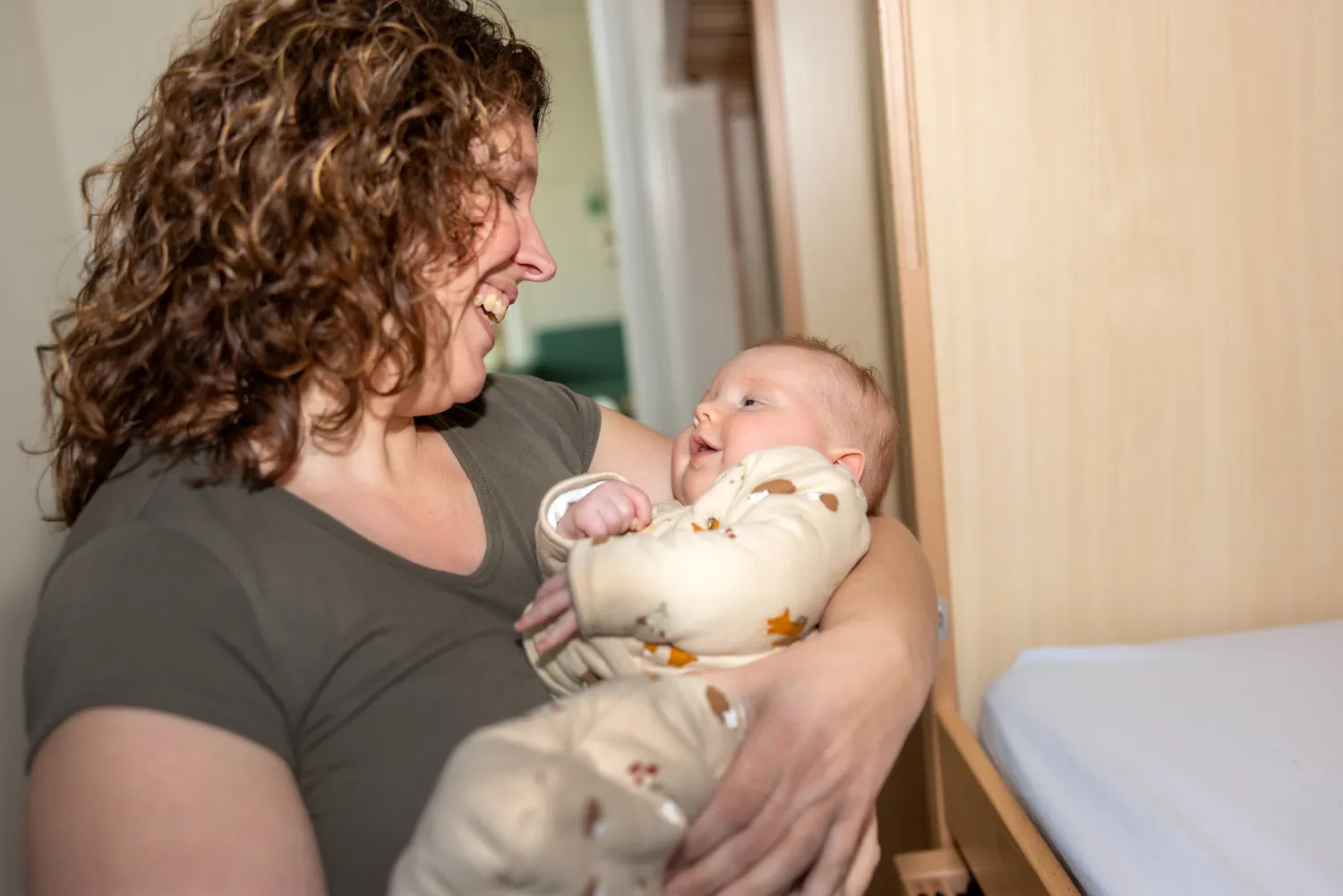 Baby kijkt liefdevol naar pedagogisch medewerker bij kinderopvang Kind&co ludens
