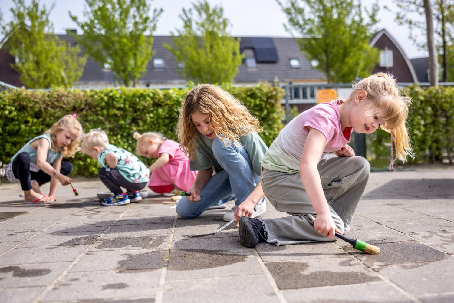 Kinderen spelen buiten op de grond met water bij kinderopvang Kind&co ludens