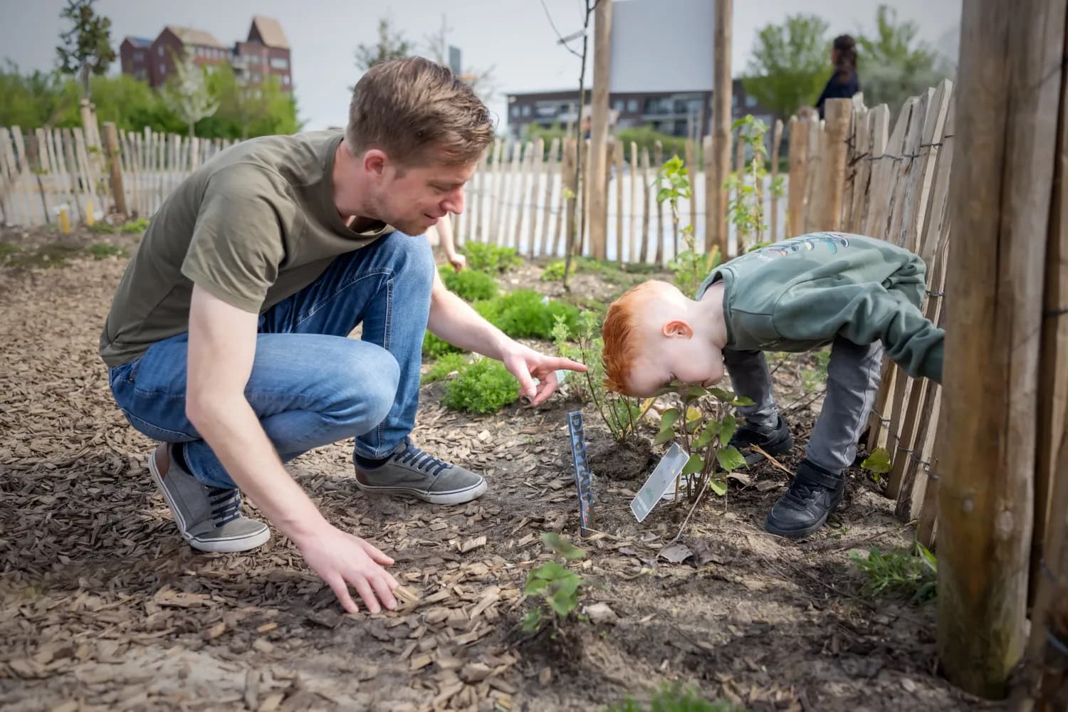Kind ruikt aan bloem in tuin met pedagogisch medewerker bij kinderopvang Kind&co ludens