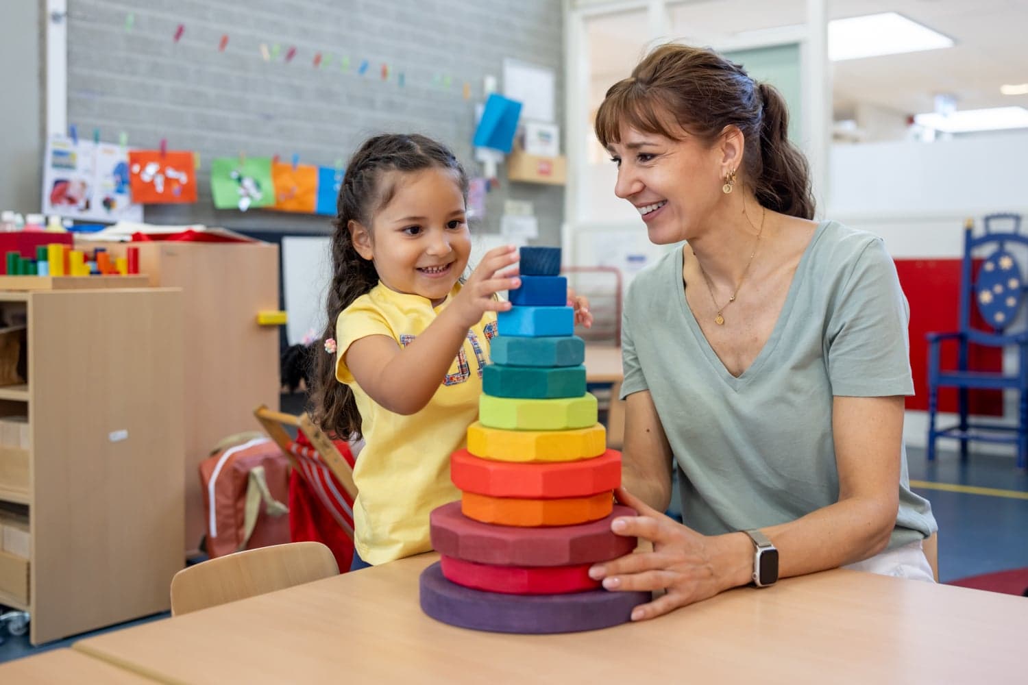 Kind stapelt houten ringen samen met pedagogisch medewerker bij kinderopvang Kind&co ludens