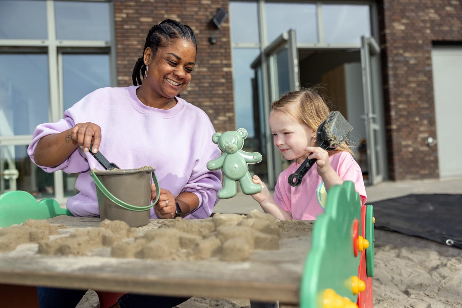 Kind maakt zandtaart in zandbak met pedagogisch medewerker bij Kind&co ludens