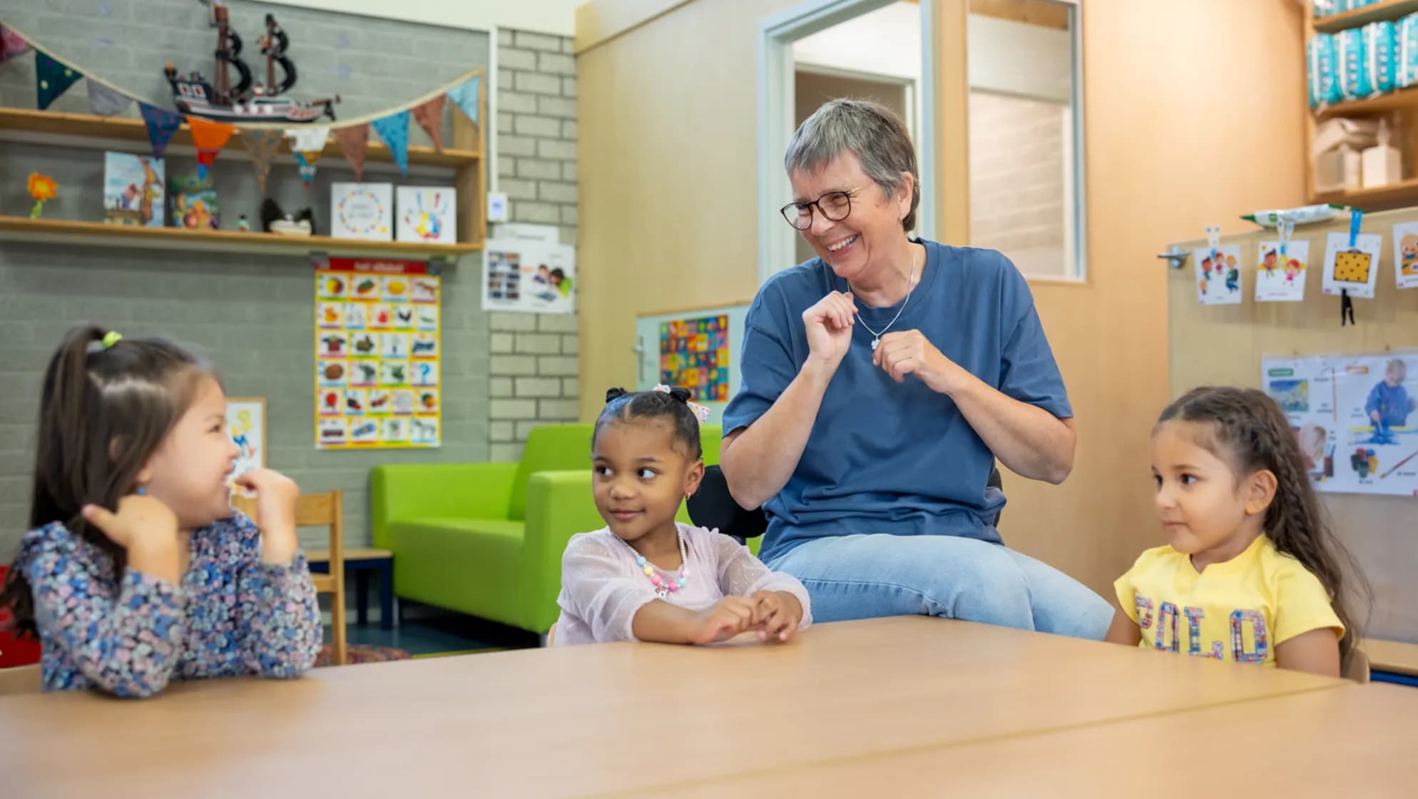 Kinderen zingen en lachen aan tafel met pedagogisch medewerker bij kinderopvang Kind&co ludens