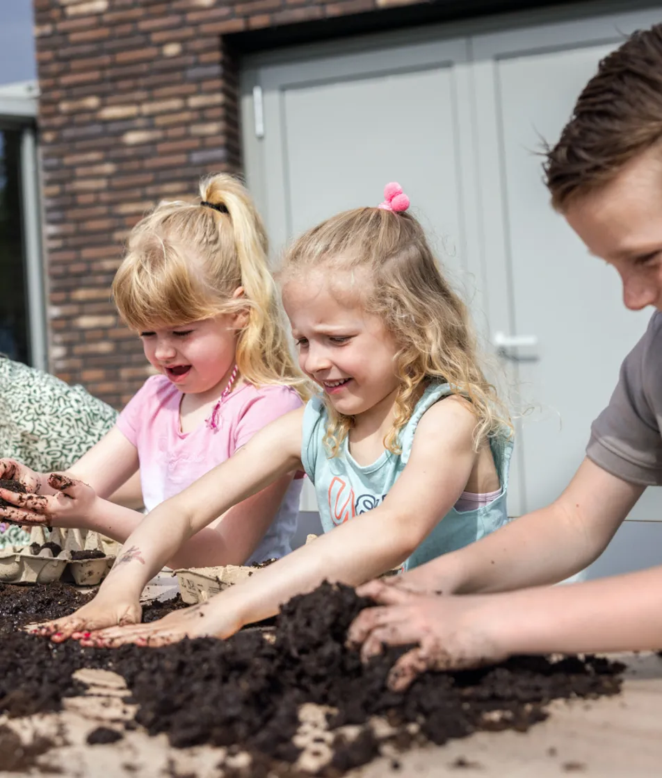 Kinderen tuinieren met pedagogisch medewerker bij kinderopvang Kind&co ludens