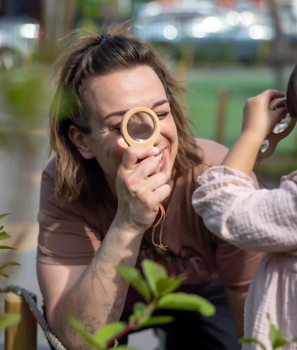 Pedagogisch medewerker en kind kijken samen door een vergrootglas  bij kinderopvang Kind&co ludens