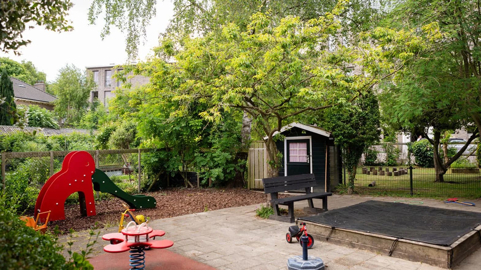 De tuin met wip, glijbaan en zandbak van peuteropvang Oog in Al bij kinderopvang Kind&co Ludens