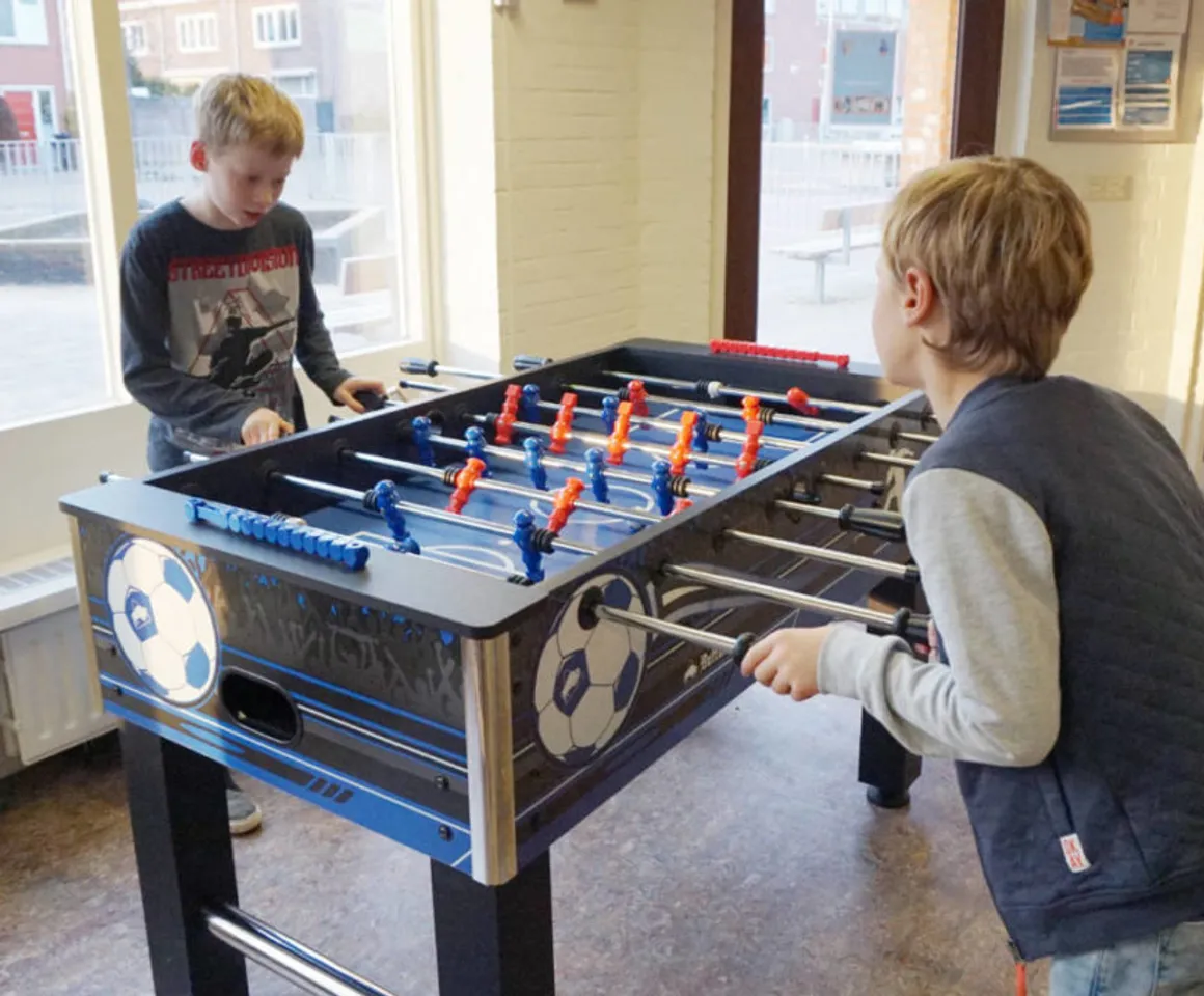 Kinderen spelen een potje voetbal aan de voetbaltafel bij buitenschoolse opvang Strandlopers bij Kind&co Ludens
