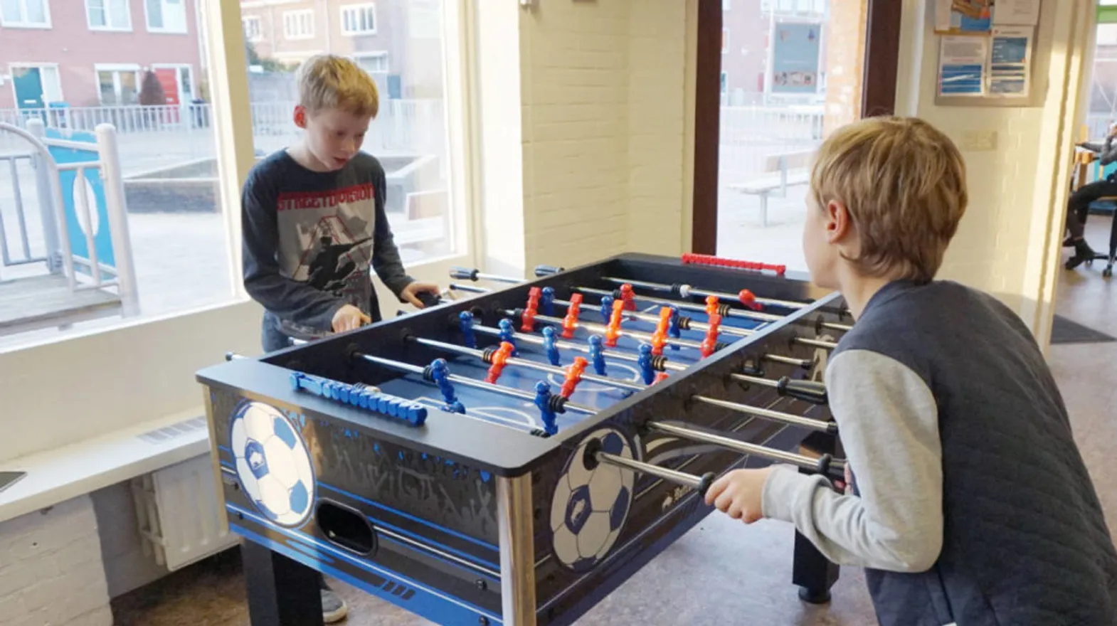 Kinderen spelen een potje voetbal aan de voetbaltafel bij buitenschoolse opvang Strandlopers bij Kind&co Ludens