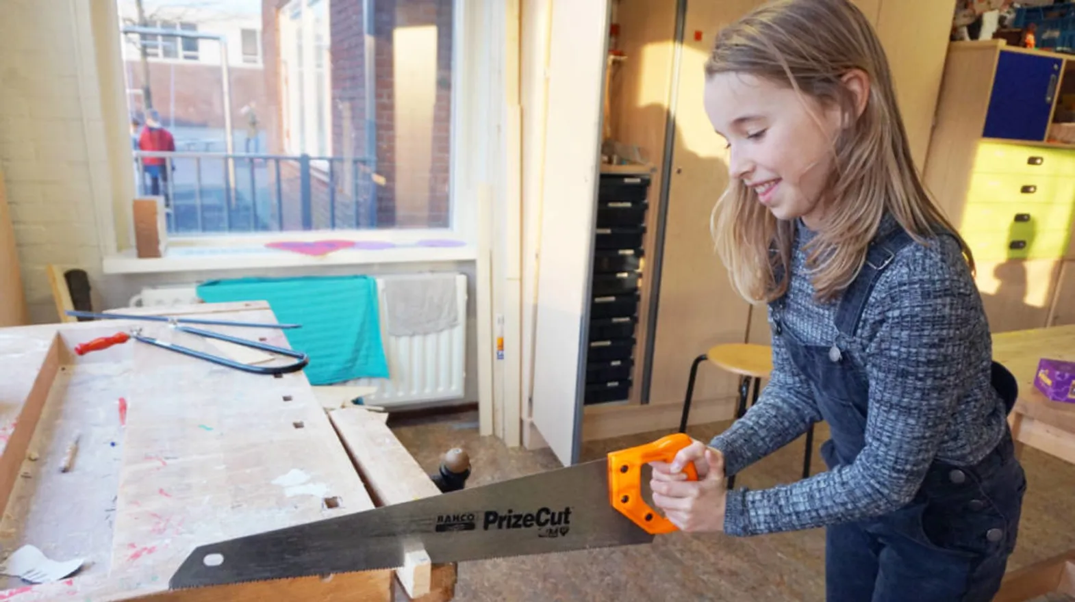 Kind zaagt in een stuk hout bij buitenschoolse opvang Strandlopers, Kind&co Ludens