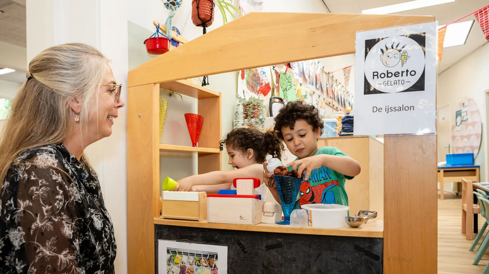 Pedagogisch medewerker speelt met de kinderen winkeltje bij PO Warmoes, kinderopvang Kind&co Ludens