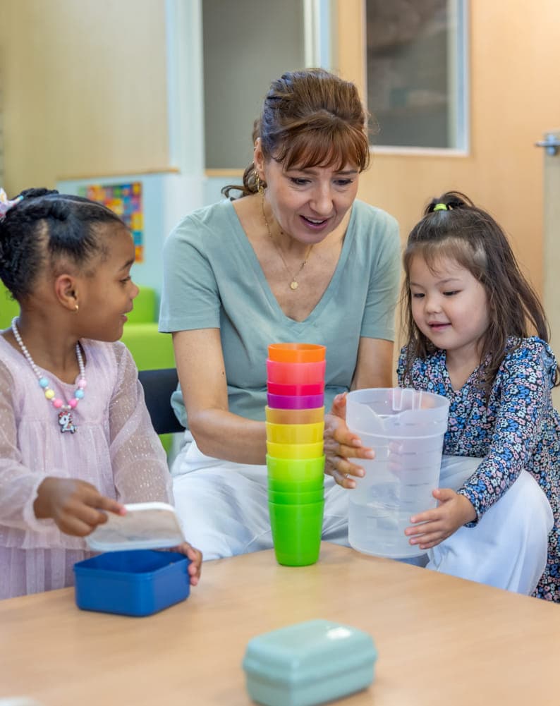 Kinderen schenken drinken in samen met pedagogisch medewerker bij kinderopvang Kind&co ludens