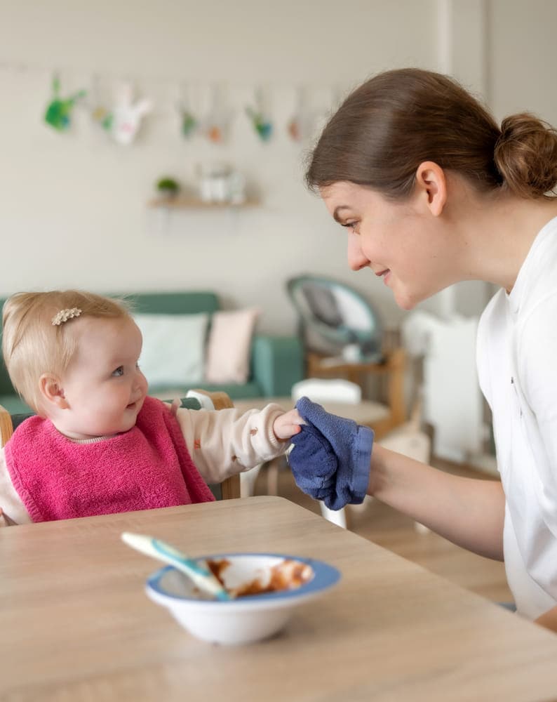 kindje wordt geholpen bij het eten door een pedagogisch medewerker bij kinderopvang Kind&co ludens