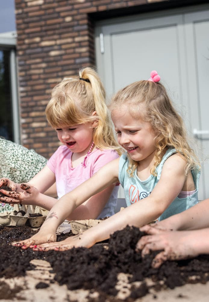 Kinderen tuinieren met pedagogisch medewerker bij kinderopvang Kind&co ludens