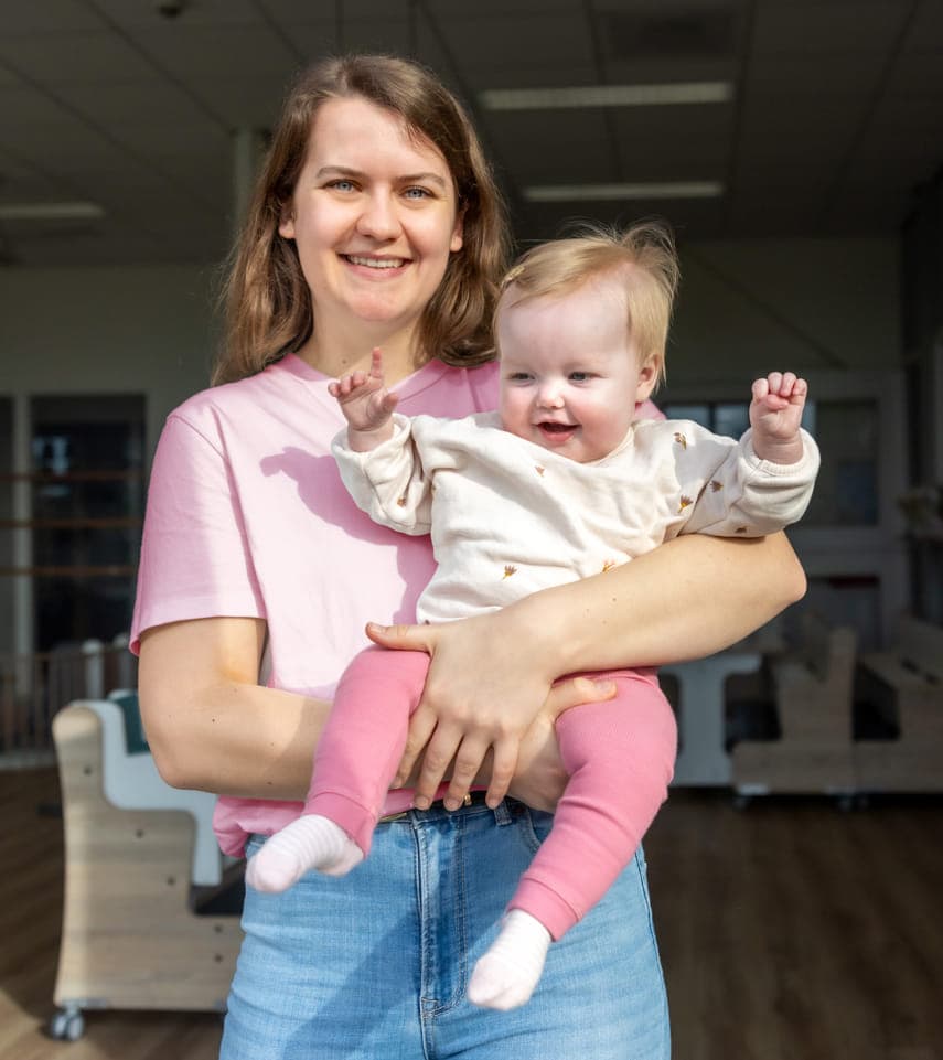 Blij kind op de armen bij een pedagogisch medewerker bij kinderopvang Kind&co ludens