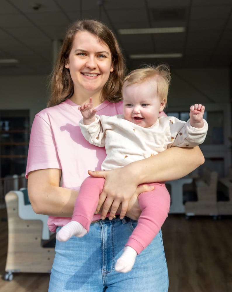 Blij kind op de armen bij een pedagogisch medewerker bij kinderopvang Kind&co ludens