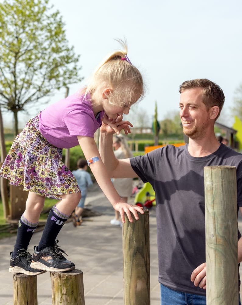 kind wordt begeleid door pedagogisch medewerker bij buitenspelen op palen bij kinderopvang Kind&co ludens