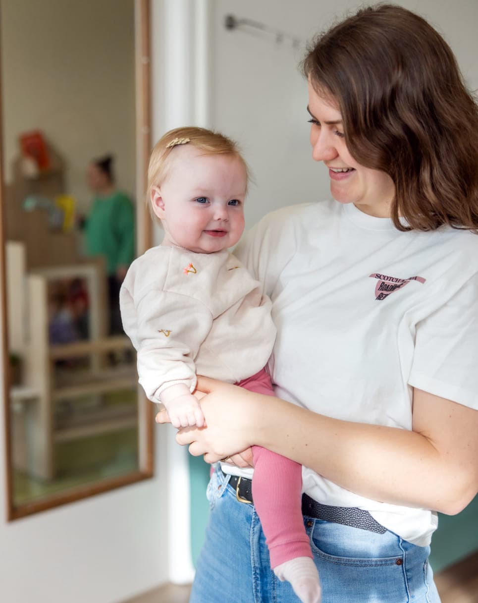 Blij kind op de arm bij een pedagogisch medewerker bij kinderopvang Kind&co ludens