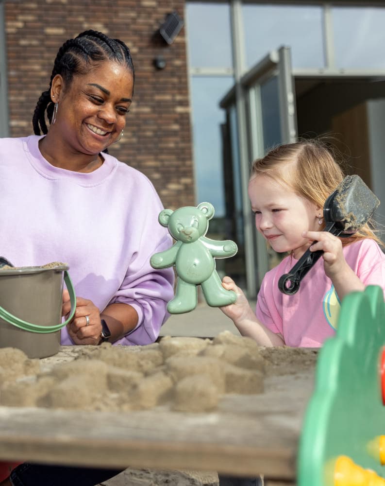 Kind maakt zandtaart in zandbak met pedagogisch medewerker bij Kind&co ludens