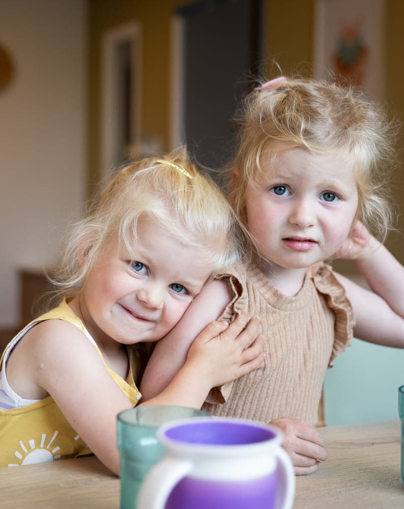 Kinderen knuffelen elkaar aan bij tafel bij kinderopvang Kind&co ludens