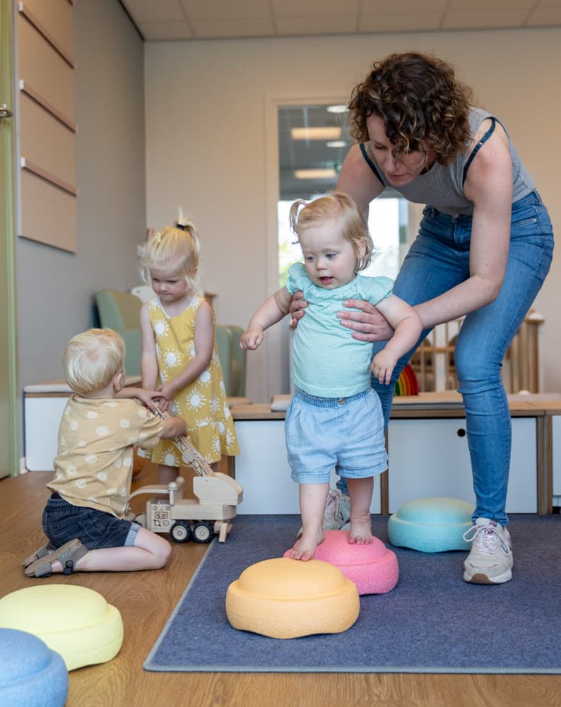 Kinderen spelen samen met pedagogisch medewerker met stapelstenen bij kinderopvang Kind&co ludens