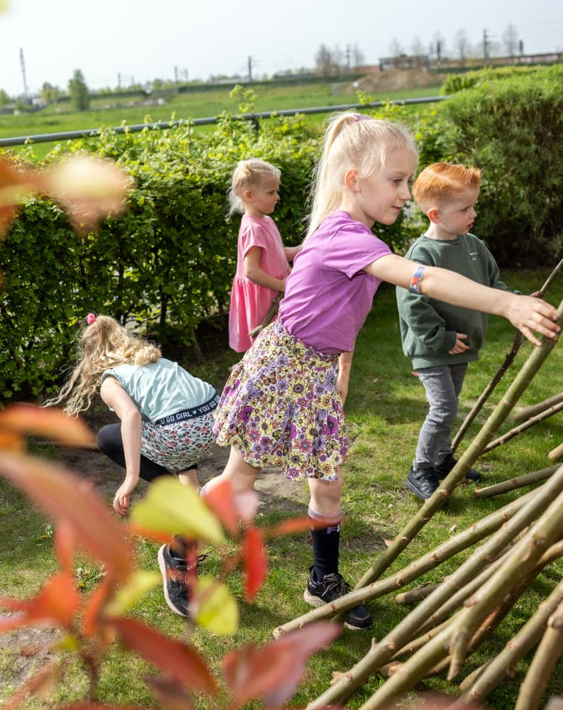 Kinderen bouwen een hut van takken bij kinderopvang Kind&co ludens