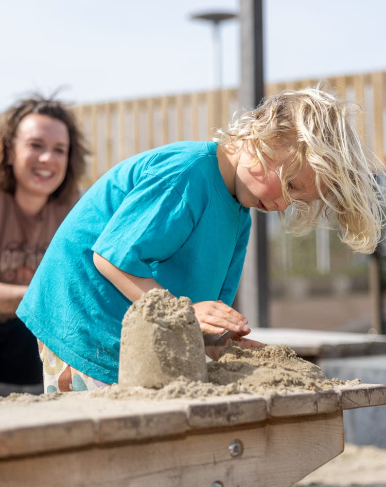 Kind maakt zandtaart in zandbak met pedagogisch medewerker bij Kind&co ludens