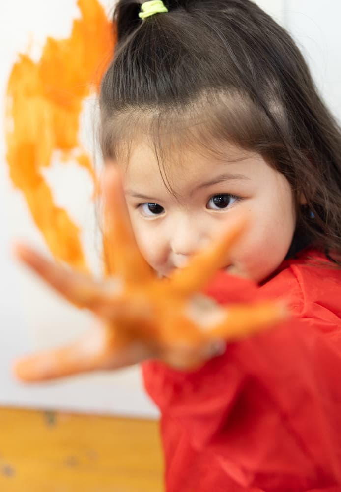 Blij kind verft met haar handen bij kinderopvang Kind&co ludens