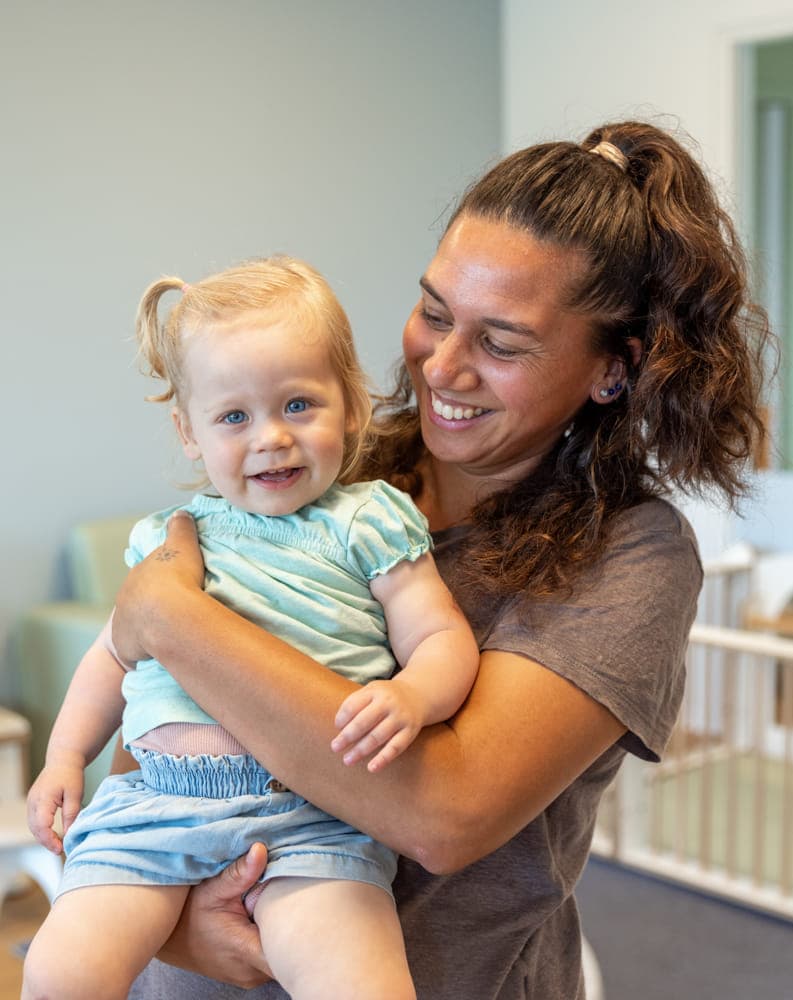 Kind wordt geknuffeld door pedagogisch medewerker bij kinderopvang Kind&co ludens