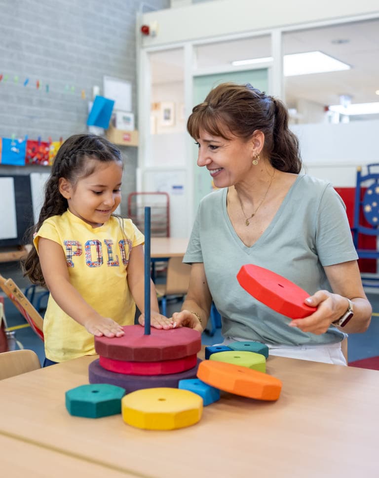 Kind stapelt houten ringen samen met pedagogisch medewerker bij kinderopvang Kind&co ludens