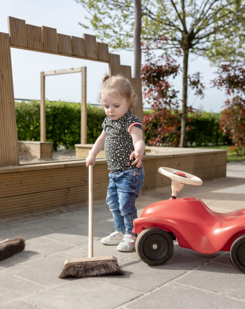 Kind speelt buiten met een bezem bij kinderopvang Kind&co ludens