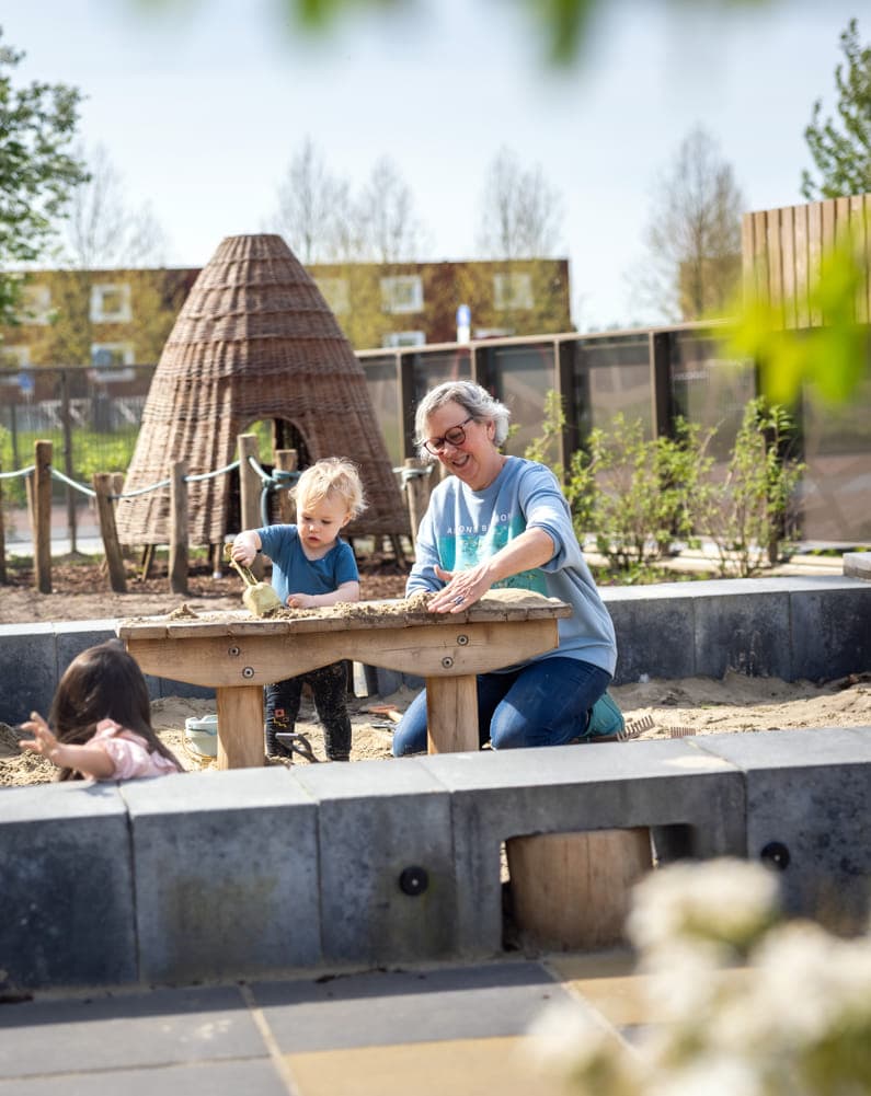 Kinderen spelen samen in de zandbak met pedagogisch medewerkers bij kinderopvang Kind&co ludens
