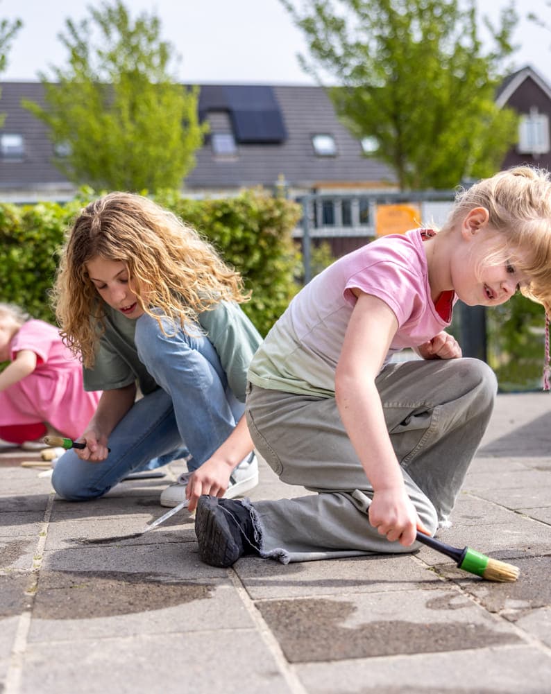 Kinderen spelen buiten op de grond met water bij kinderopvang Kind&co ludens