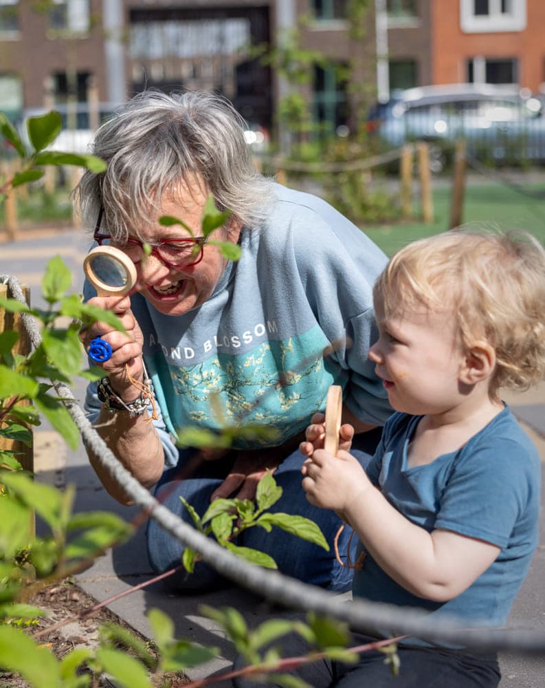 Pedagogisch medewerker en kind kijken samen door een loep naar blaadjes bij kinderopvang Kind&co ludens