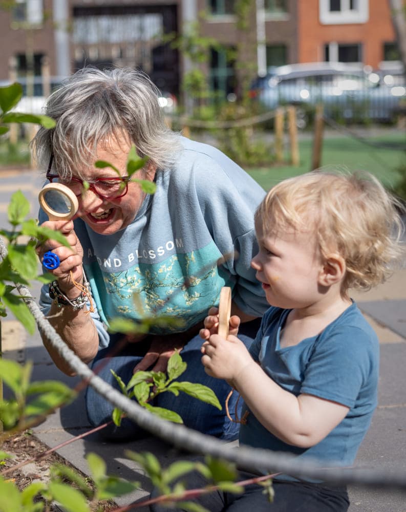 Pedagogisch medewerker en kind kijken samen door een loep naar blaadjes bij kinderopvang Kind&co ludens