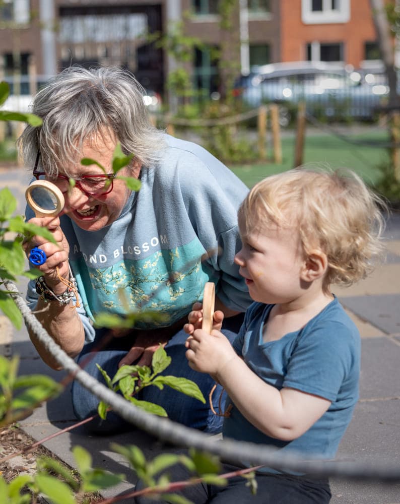 Pedagogisch medewerker en kind kijken samen door een loep naar blaadjes bij kinderopvang Kind&co ludens