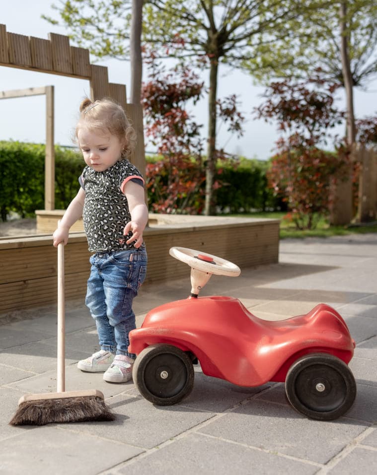 Kind speelt buiten met een bezem bij kinderopvang Kind&co ludens