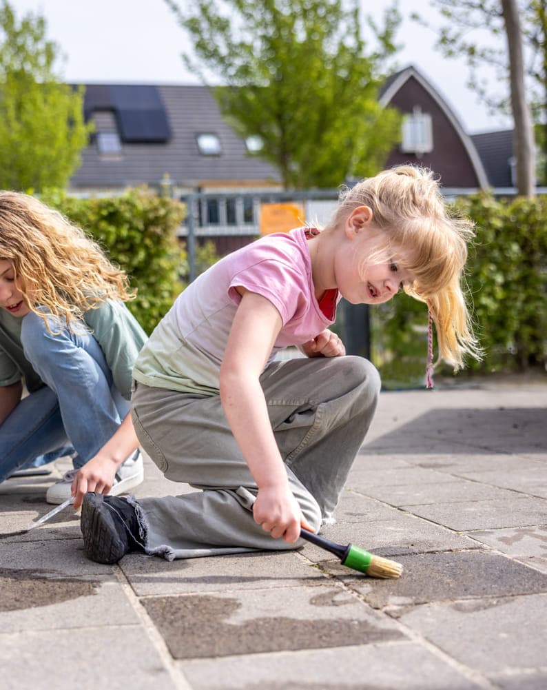 Kinderen spelen buiten op de grond met water bij kinderopvang Kind&co ludens