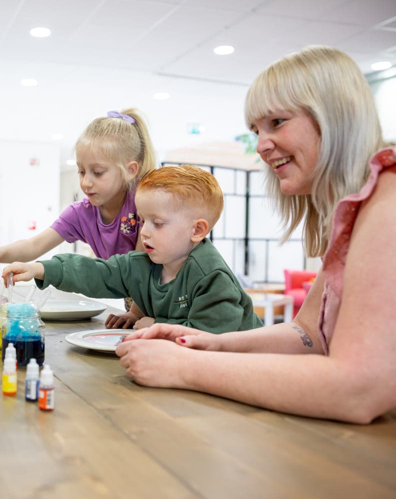 kinderen worden door een pedagogisch medewerker begeleid met het verven bij kinderopvang Kind&co ludens