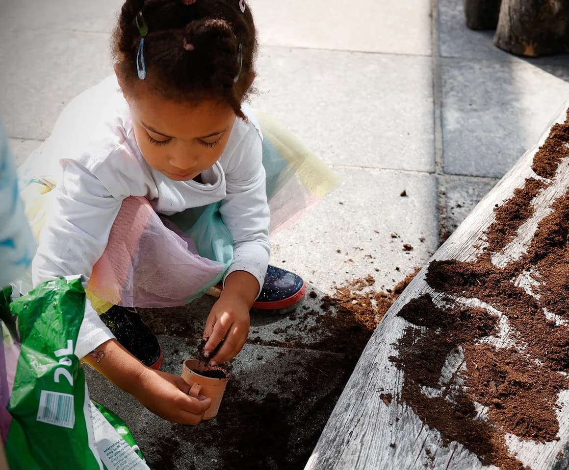 Kind van de peutergroep poot zaadjes in de moestuin bij kinderopvang Kind&co ludens