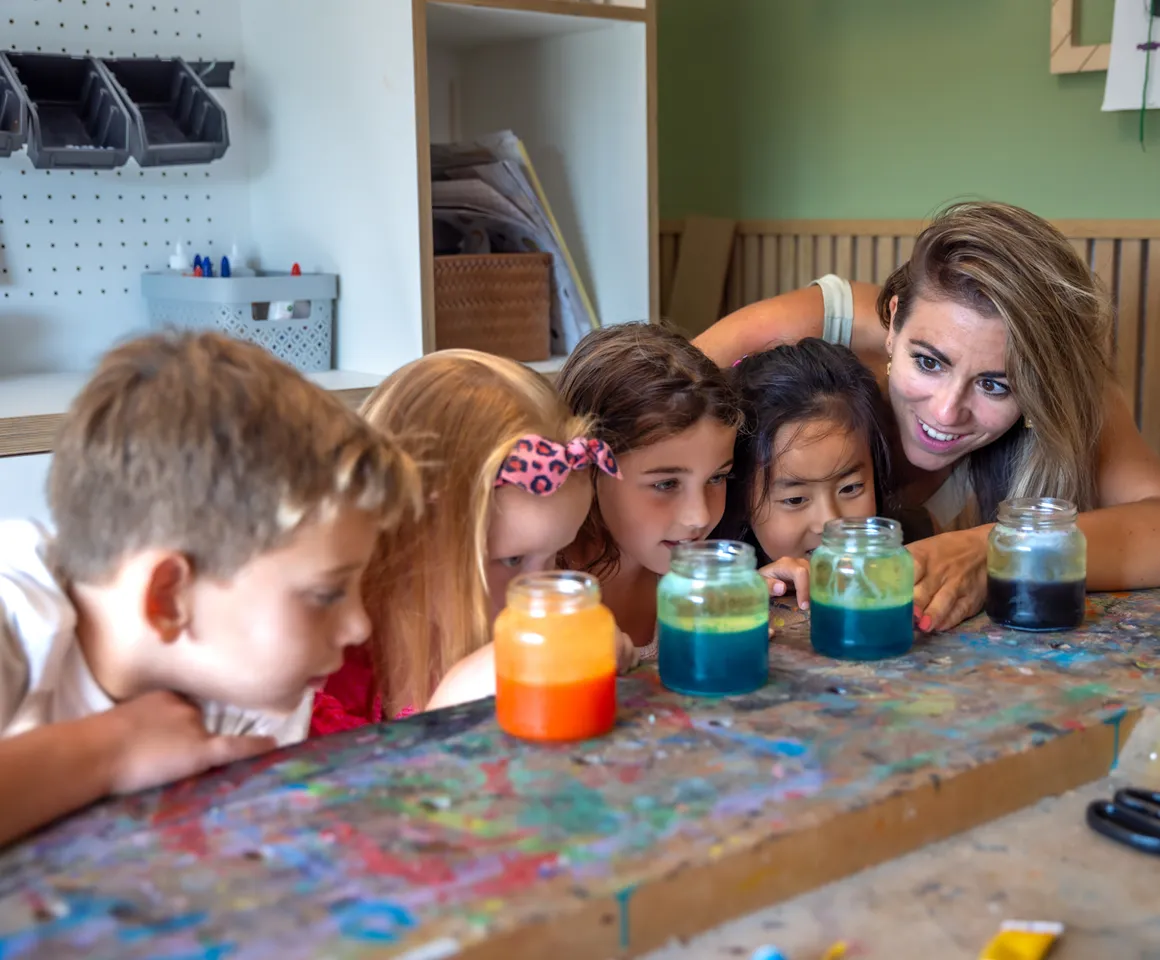 Kinderen kijken met pedagogisch medewerker naar pot met gekleurd water bij kinderopvang Kind&co ludens