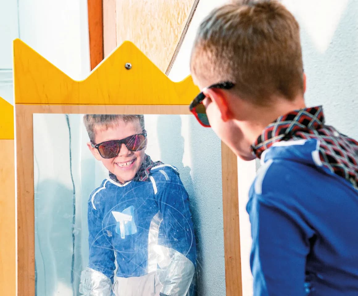 Kind op de BSO heeft veel plezier tijdens een verkleedpartij bij het kijken in de spiegel van kinderopvang Kind&co ludens