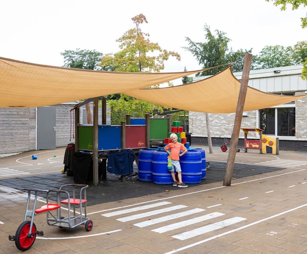 Kind buiten onder het schaduwdoek bij BSO Orangerie Baarn van Kinderopvang Kind&co ludens