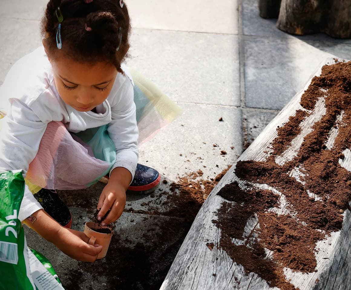 Kind van de peutergroep poot zaadjes in de moestuin bij kinderopvang Kind&co ludens