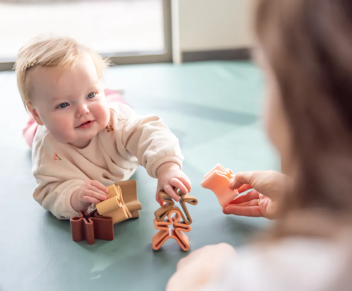 Baby speelt met  houten speelgoed poppetjes bij gastouder van kinderopvang Kind&co ludens