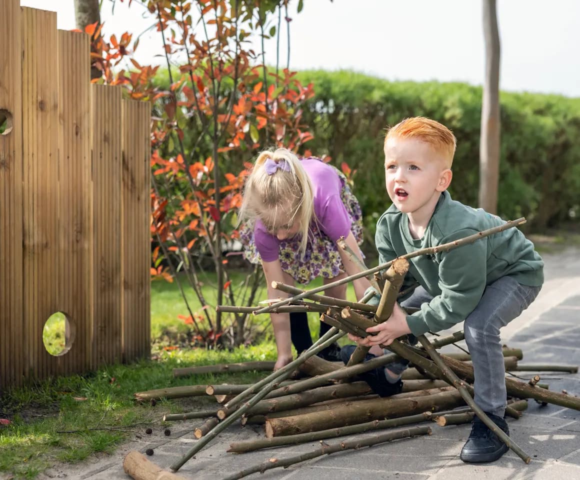 Kinderen spelen met takken buiten bij kinderopvang Kind&co ludens