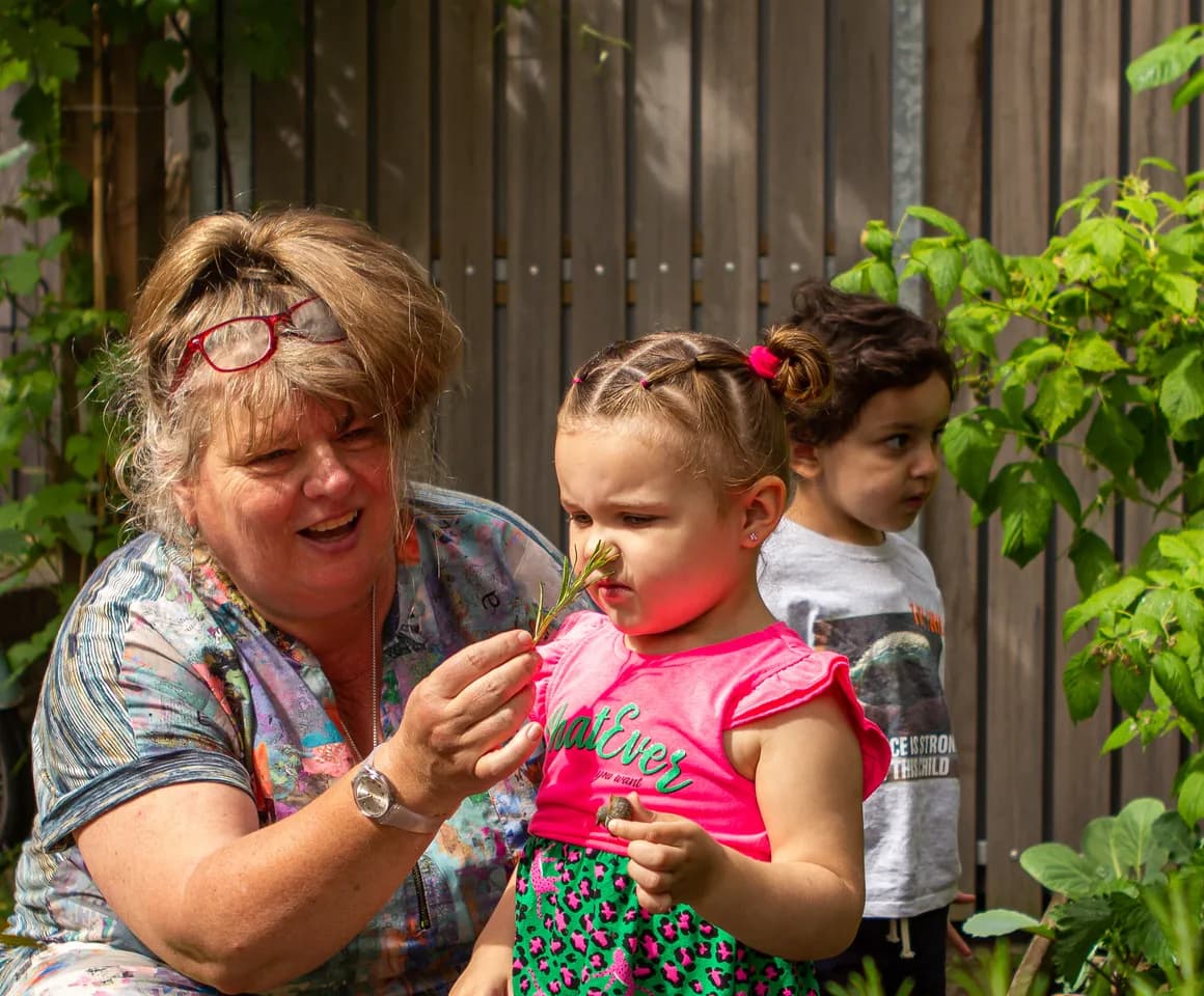 Kind ruikt aan plant in moestuin bij peuteropvang 't Egeltje, Kind&co ludens