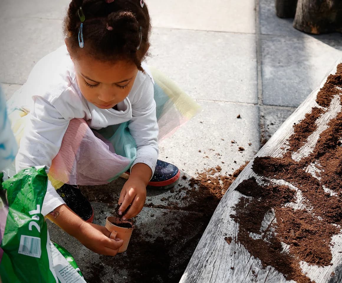 Kind van de peutergroep poot zaadjes in de moestuin bij kinderopvang Kind&co ludens