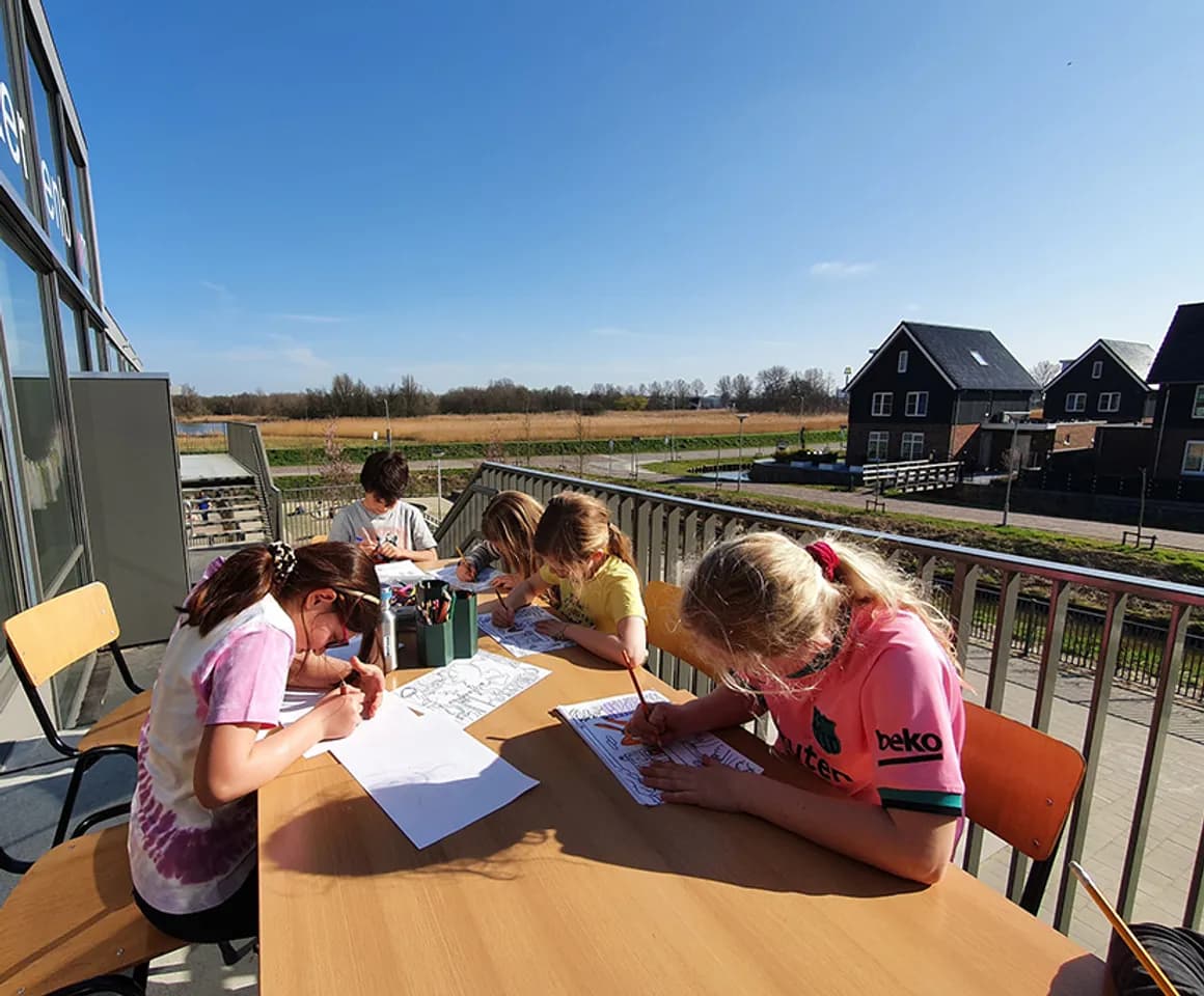Kinderen schrijvend aan tafel in de buitenruimte bij BSO-Kersenbende van kinderopvang Kind&co ludens